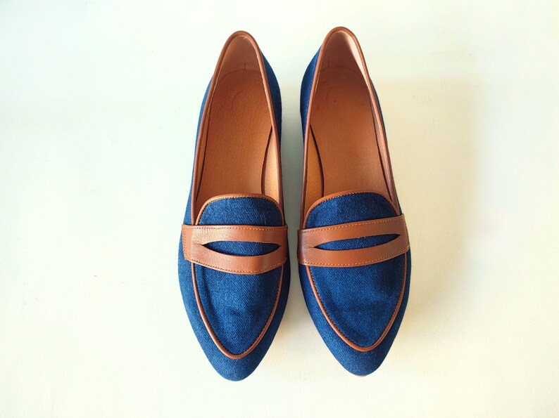 May include: A pair of blue denim loafers with brown leather accents. The loafers have a pointed toe and a slip-on design.