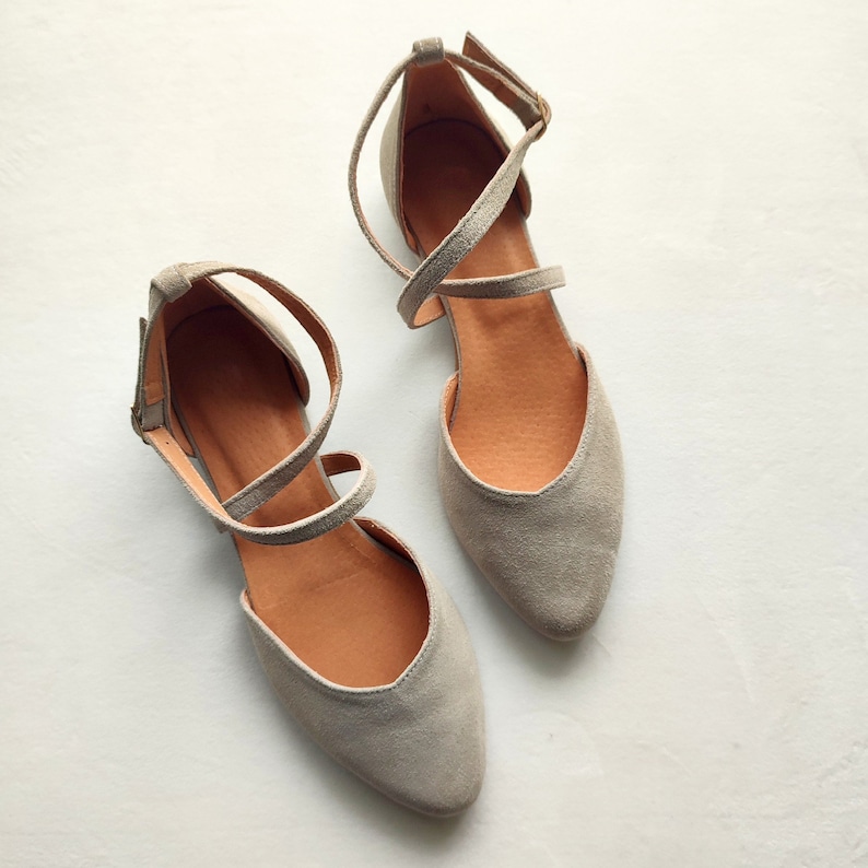 May include: A pair of gray suede ballet flats with criss-cross straps. The flats have a pointed toe and a low heel.