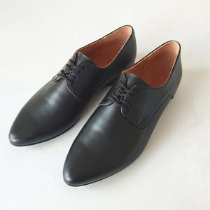 May include: A pair of black leather dress shoes with a classic lace-up design. The shoes have a pointed toe and a smooth, polished finish. The interior lining is a light brown color.