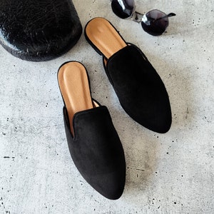 K&ouml;nnte beinhalten: Ein Paar schwarze Wildlederslipper mit spitzer Zehenpartie und niedrigem Absatz. Die Slipper haben eine braune Ledersohle.