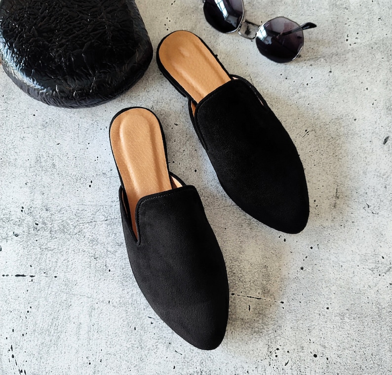 K&ouml;nnte beinhalten: Ein Paar schwarze Wildlederslipper mit spitzer Zehenpartie und niedrigem Absatz. Die Slipper haben eine braune Ledersohle.