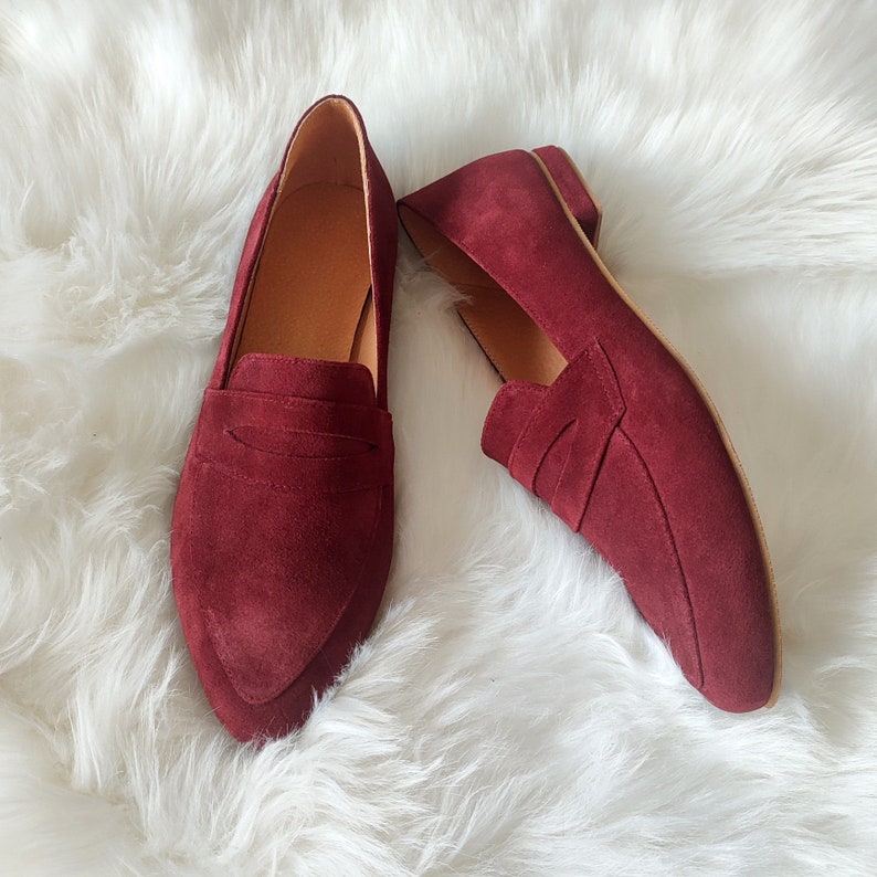 May include: A pair of burgundy suede loafers with a pointed toe and a simple design.