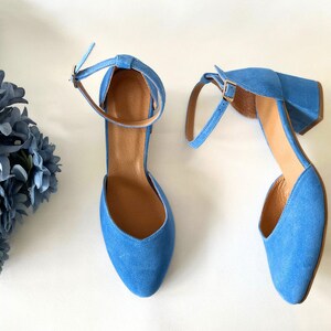 May include: A pair of blue suede heeled shoes with ankle straps. The shoes have a pointed toe and a block heel.