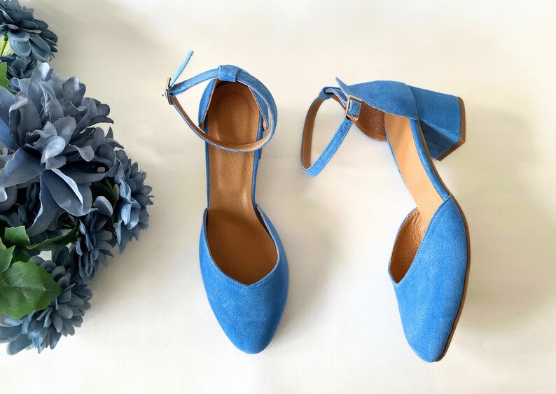 May include: A pair of blue suede heeled shoes with ankle straps. The shoes have a pointed toe and a block heel.