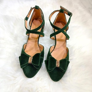 May include: A pair of dark green velvet heeled shoes with a bow detail and rhinestone embellishments.