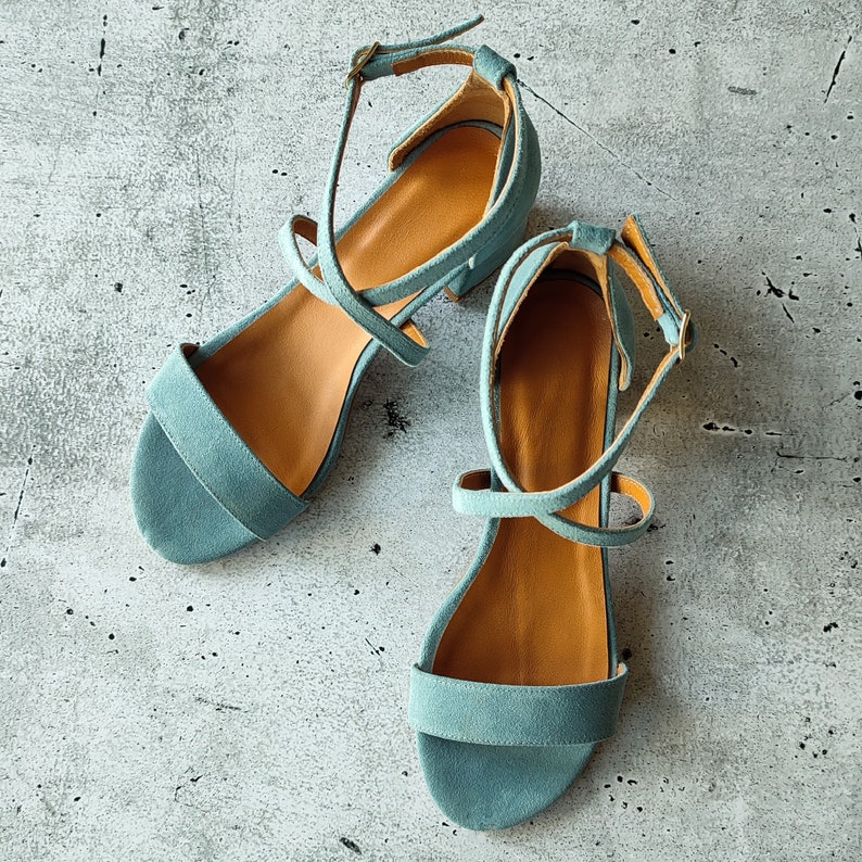 May include: A pair of light blue suede heeled sandals with criss-cross straps.