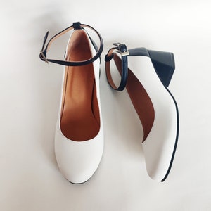 May include: A pair of white heeled shoes with black ankle straps and black heels.