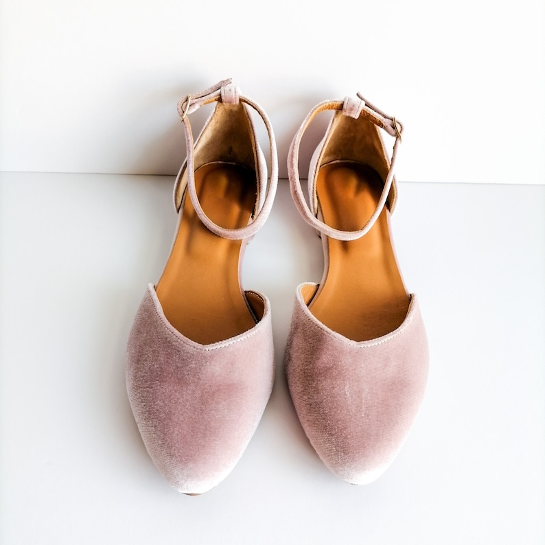 May include: A pair of dusty rose velvet flats with ankle straps. The straps have a buckle closure.