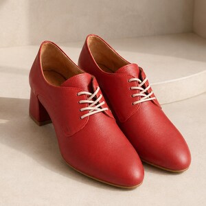 May include: A pair of red leather oxford shoes with white laces. The shoes have a rounded toe and a block heel. The heel height is approximately 2.5 inches.