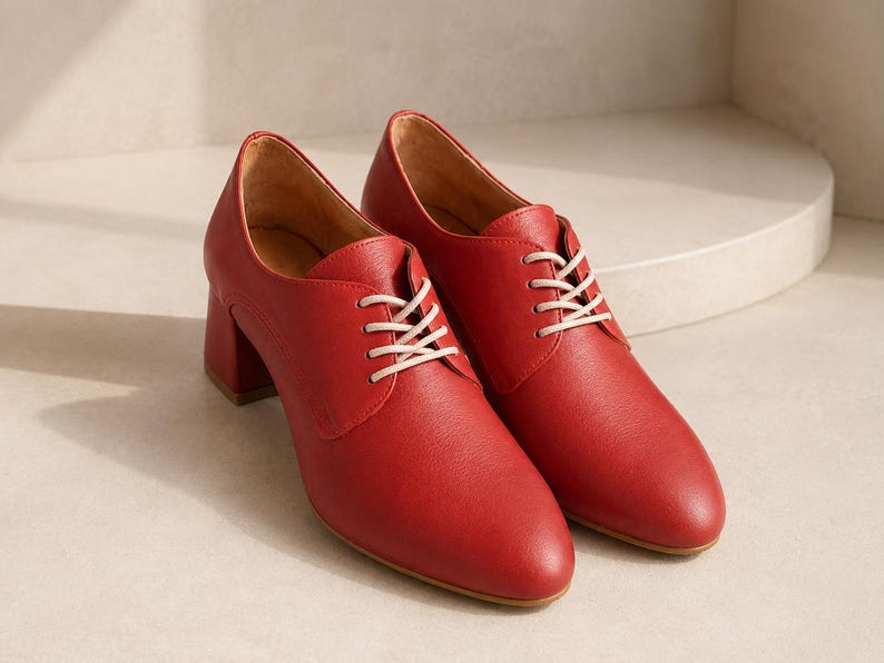 May include: A pair of red leather oxford shoes with white laces. The shoes have a rounded toe and a block heel. The heel height is approximately 2.5 inches.