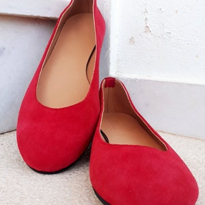 May include: A pair of red suede ballet flats with a rounded toe and black soles.