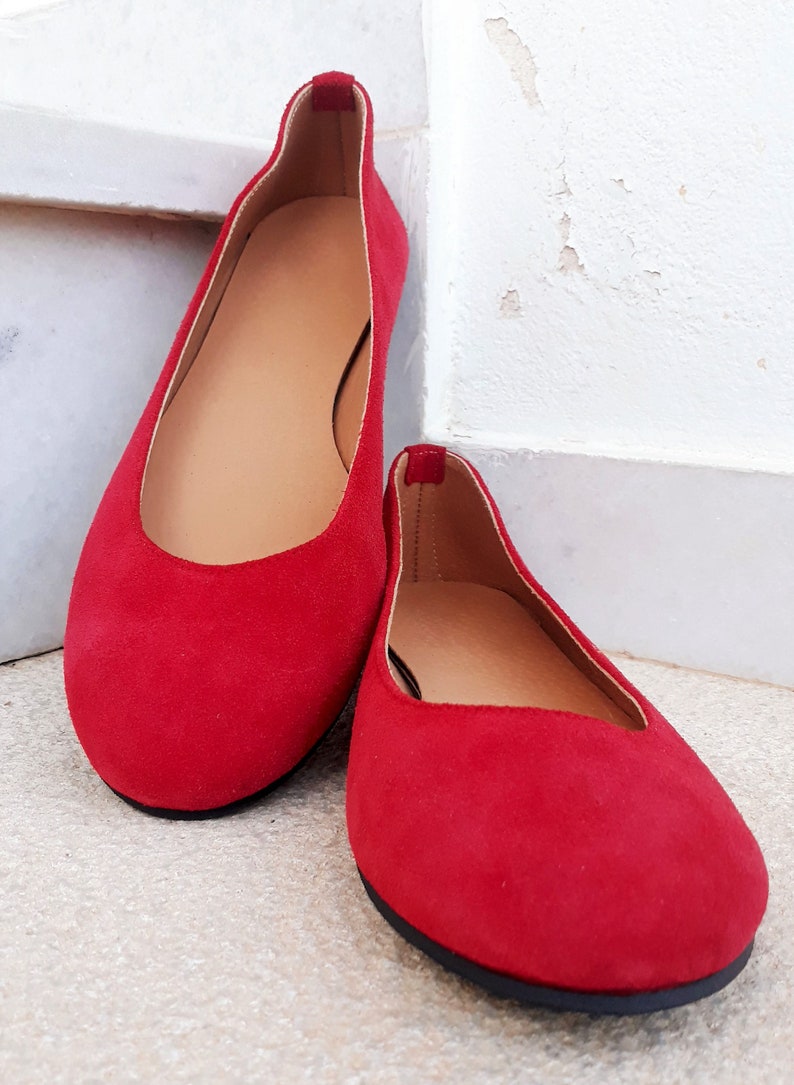 May include: A pair of red suede ballet flats with a rounded toe and black soles.
