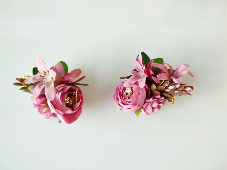 May include: Two pink flower arrangements with green leaves and gold accents. The flowers are arranged in a cluster and are perfect for adding a touch of elegance to any occasion.