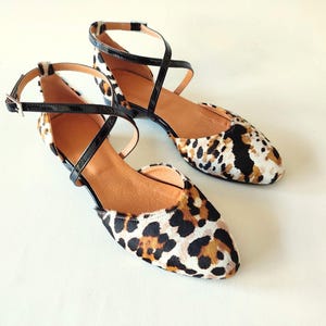 May include: A pair of black and brown leopard print ballet flats with criss-cross straps.