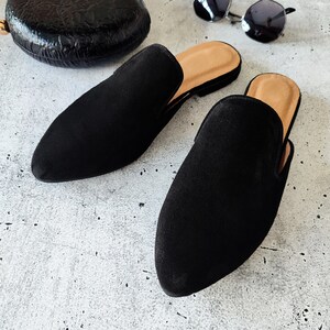 K&ouml;nnte beinhalten: Ein Paar schwarze Wildlederslipper mit spitzer Zehenpartie. Die Slipper haben einen niedrigen Absatz und eine bequeme Passform.