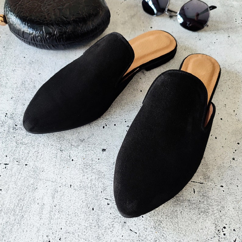 K&ouml;nnte beinhalten: Ein Paar schwarze Wildlederslipper mit spitzer Zehenpartie. Die Slipper haben einen niedrigen Absatz und eine bequeme Passform.