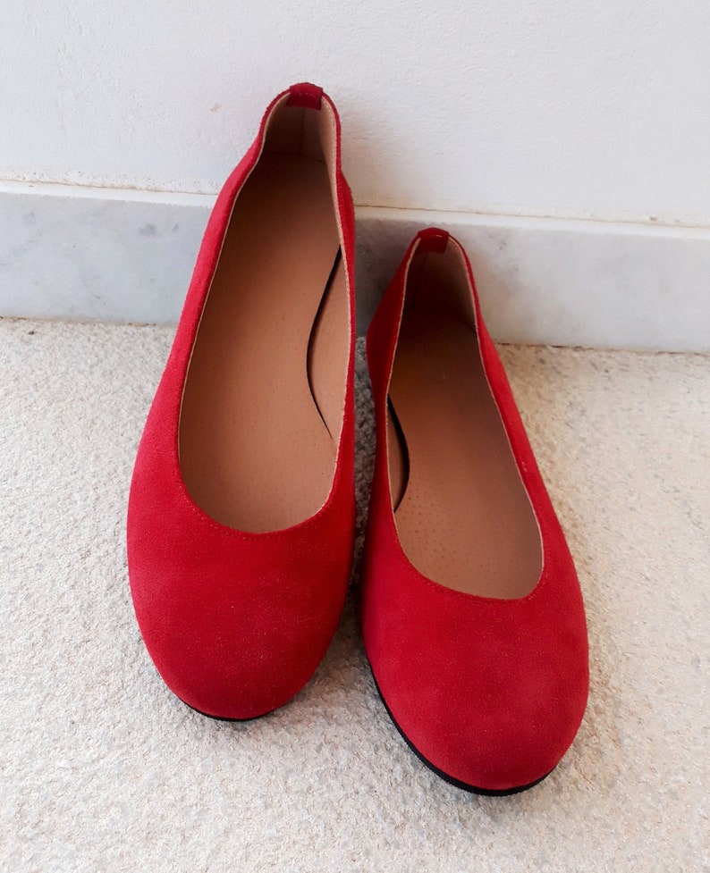 May include: A pair of red suede ballet flats. The flats have a rounded toe and a simple design.