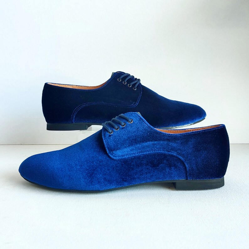 May include: A pair of blue velvet lace-up shoes. The shoes have a low heel and a pointed toe.