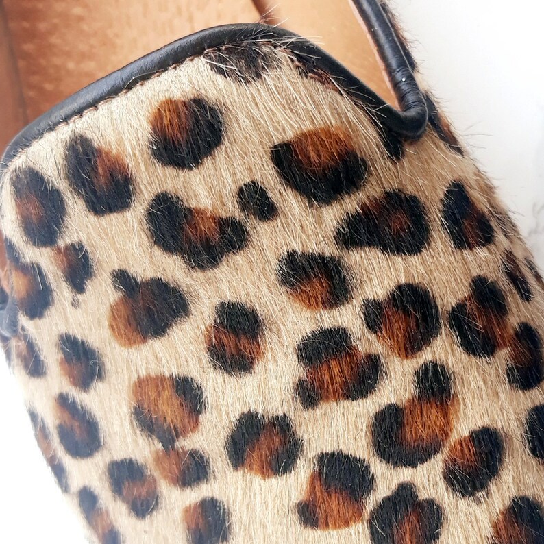 May include: Close-up of a brown and black leopard print fabric with a black leather trim. The fabric is soft and fuzzy.