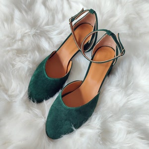 K&ouml;nnte beinhalten: Ein Paar dunkelgr&uuml;ne Wildlederschuhe mit Kn&ouml;chelriemen. Die Schuhe haben eine spitze Zehenpartie und einen niedrigen Absatz.