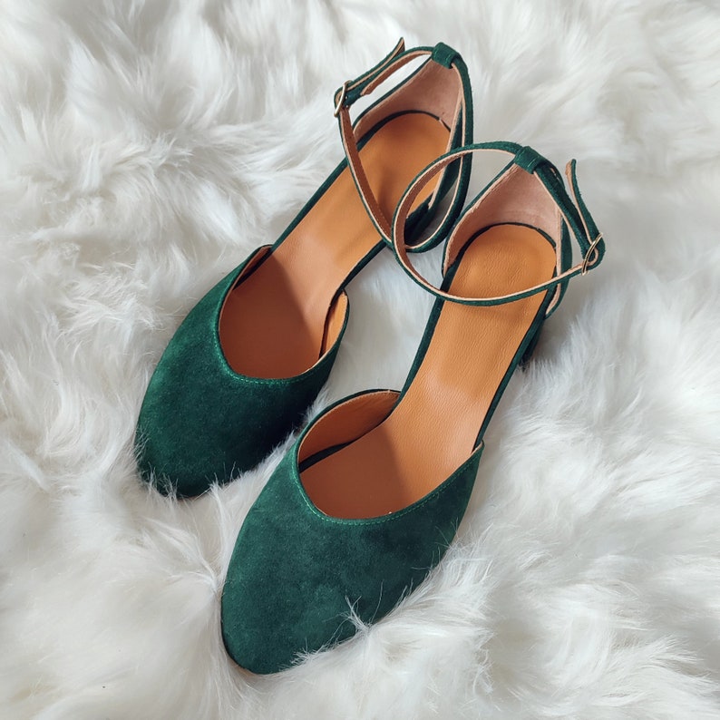 K&ouml;nnte beinhalten: Ein Paar dunkelgr&uuml;ne Wildlederschuhe mit Kn&ouml;chelriemen. Die Schuhe haben eine spitze Zehenpartie und einen niedrigen Absatz.