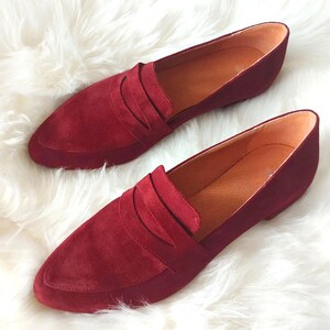 May include: A pair of burgundy suede loafers with a pointed toe and a single strap across the vamp.
