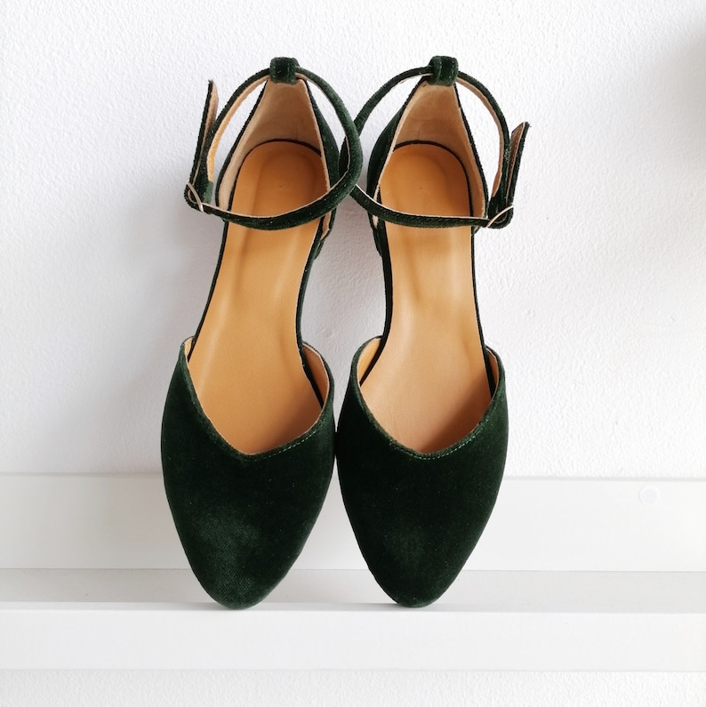 May include: A pair of dark green velvet ankle strap flats with a pointed toe.