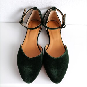 May include: A pair of dark green velvet ankle strap flats with a pointed toe.