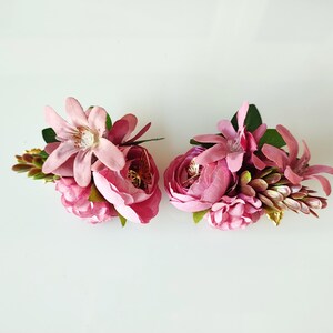 May include: Two pink flower arrangements with a mix of pink flowers and greenery. The flowers are artificial and are arranged in a cluster.