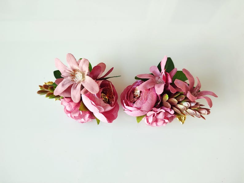 May include: Two pink flower arrangements with a mix of pink flowers and greenery. The flowers are artificial and are arranged in a cluster.