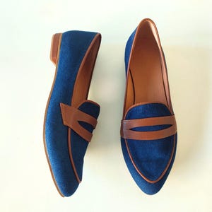 May include: A pair of blue denim loafers with brown leather accents. The loafers have a pointed toe and a low heel.