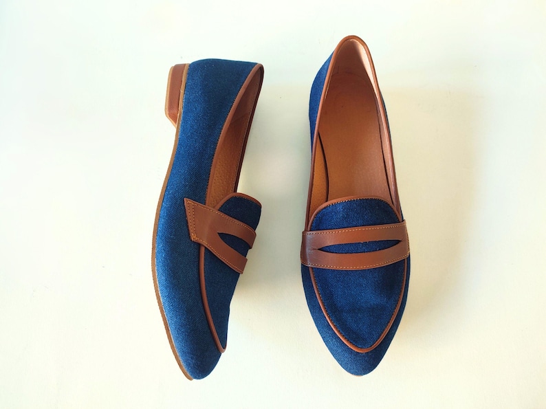 May include: A pair of blue denim loafers with brown leather accents. The loafers have a pointed toe and a low heel.