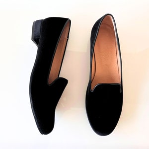 K&ouml;nnte beinhalten: Ein Paar schwarze Samt-Slipper mit niedrigem Absatz. Die Slipper haben eine spitze Zehenpartie und ein schlichtes Design.