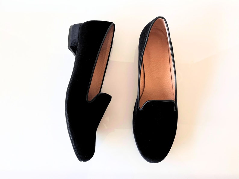 K&ouml;nnte beinhalten: Ein Paar schwarze Samt-Slipper mit niedrigem Absatz. Die Slipper haben eine spitze Zehenpartie und ein schlichtes Design.