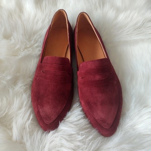 May include: A pair of burgundy suede loafers with a pointed toe.