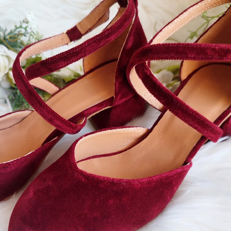 May include: A pair of burgundy velvet heeled shoes with ankle straps. The shoes have a pointed toe and a low block heel.