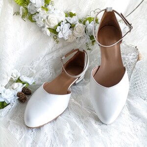 May include: A pair of white leather ankle strap shoes with a pointed toe. The shoes are on a white lace background.