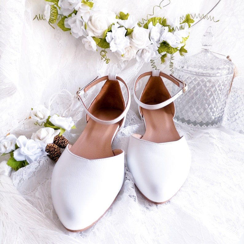 May include: A pair of white leather pointed-toe flats with ankle straps. The shoes are on a white lace background.