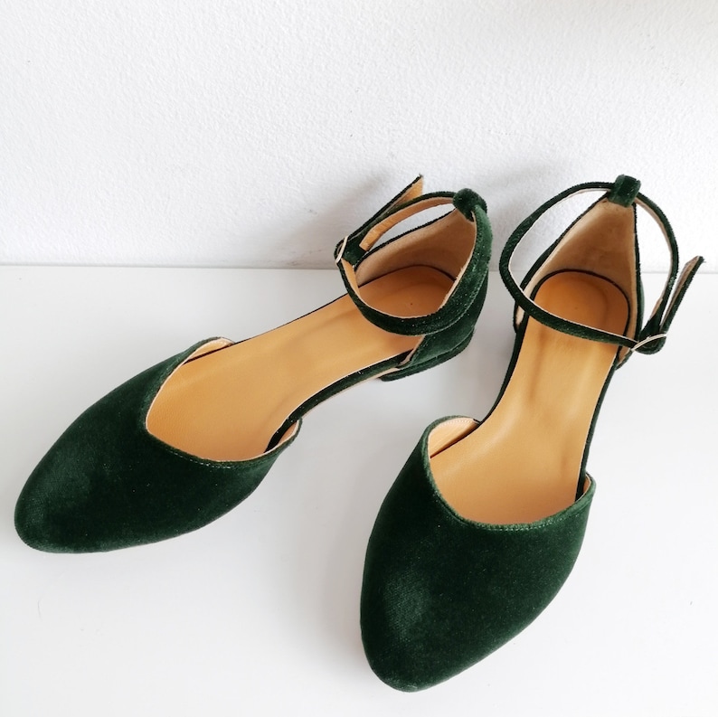 May include: A pair of dark green velvet ankle strap flats with a pointed toe.