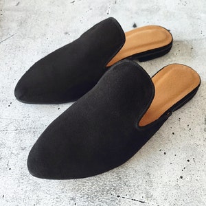 K&ouml;nnte beinhalten: Ein Paar schwarze Wildlederschlappen mit spitzer Zehenpartie und niedrigem Absatz. Die Schlappen haben ein schlichtes Design und sind aus weichem, bequemem Material gefertigt.