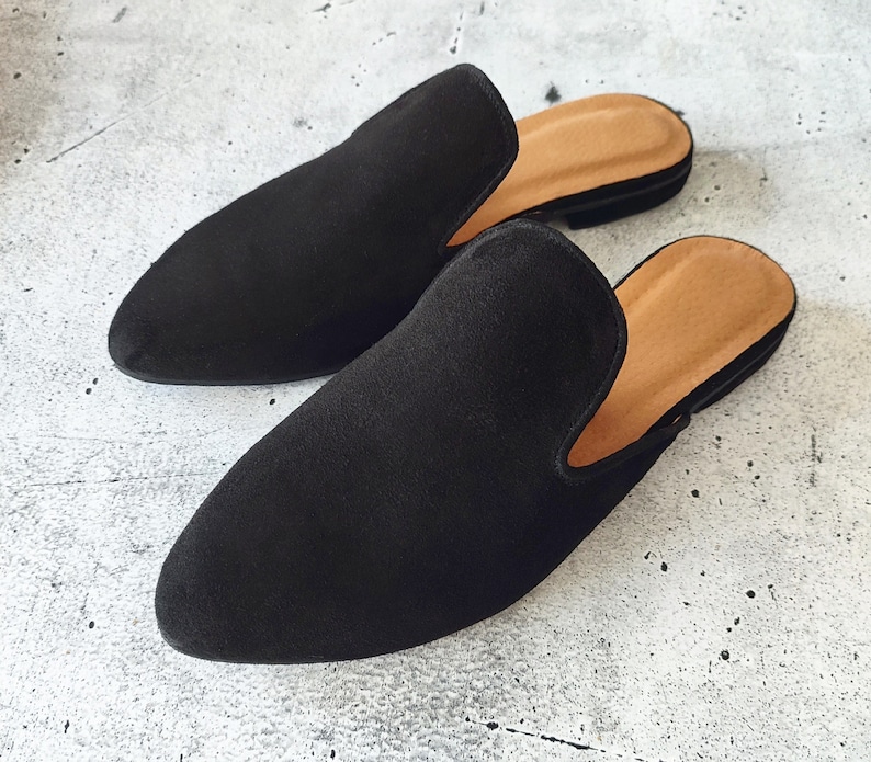 K&ouml;nnte beinhalten: Ein Paar schwarze Wildlederschlappen mit spitzer Zehenpartie und niedrigem Absatz. Die Schlappen haben ein schlichtes Design und sind aus weichem, bequemem Material gefertigt.