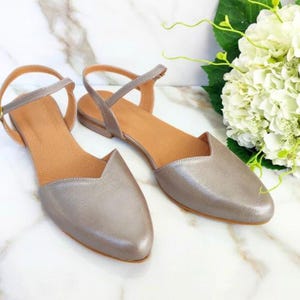 Op de afbeelding: Een paar zilveren metallic spitsschoenen met enkelbandjes. De schoenen hebben een eenvoudig ontwerp en zijn perfect voor een casual of chique gelegenheid.