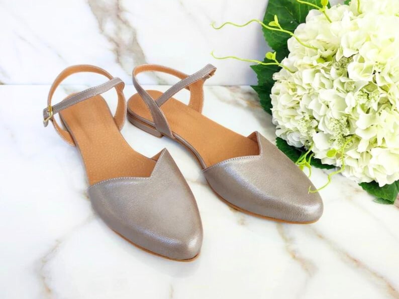Op de afbeelding: Een paar zilveren metallic spitsschoenen met enkelbandjes. De schoenen hebben een eenvoudig ontwerp en zijn perfect voor een casual of chique gelegenheid.