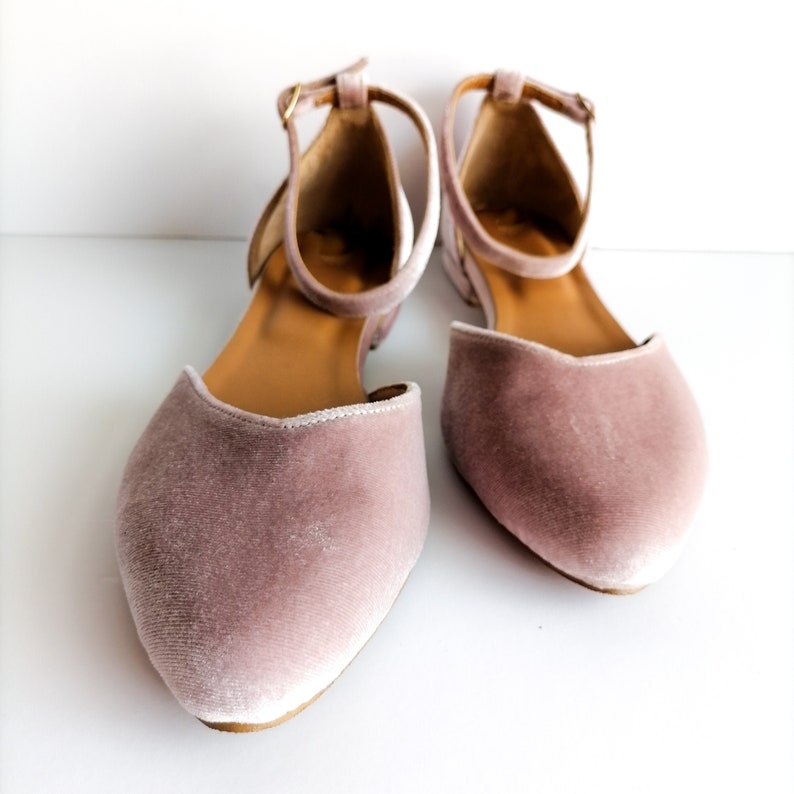 May include: A pair of dusty rose velvet ballet flats with ankle straps. The flats have a pointed toe and a low heel.