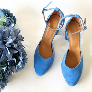 May include: A pair of blue suede heeled shoes with ankle straps. The shoes have a pointed toe and a block heel.