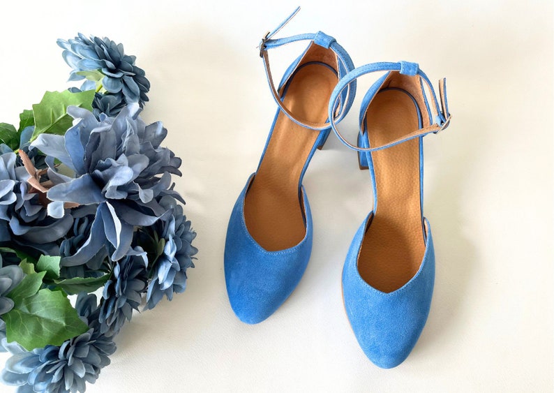 May include: A pair of blue suede heeled shoes with ankle straps. The shoes have a pointed toe and a block heel.