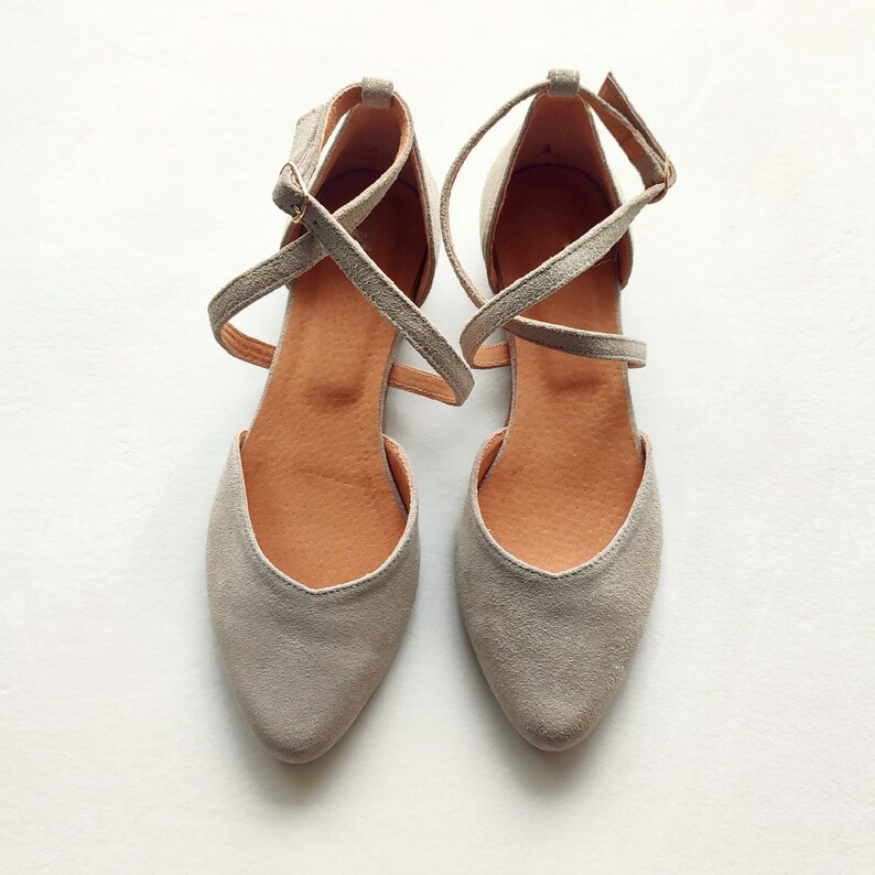 May include: A pair of gray suede ballet flats with criss-cross straps. The straps are tied at the ankle.