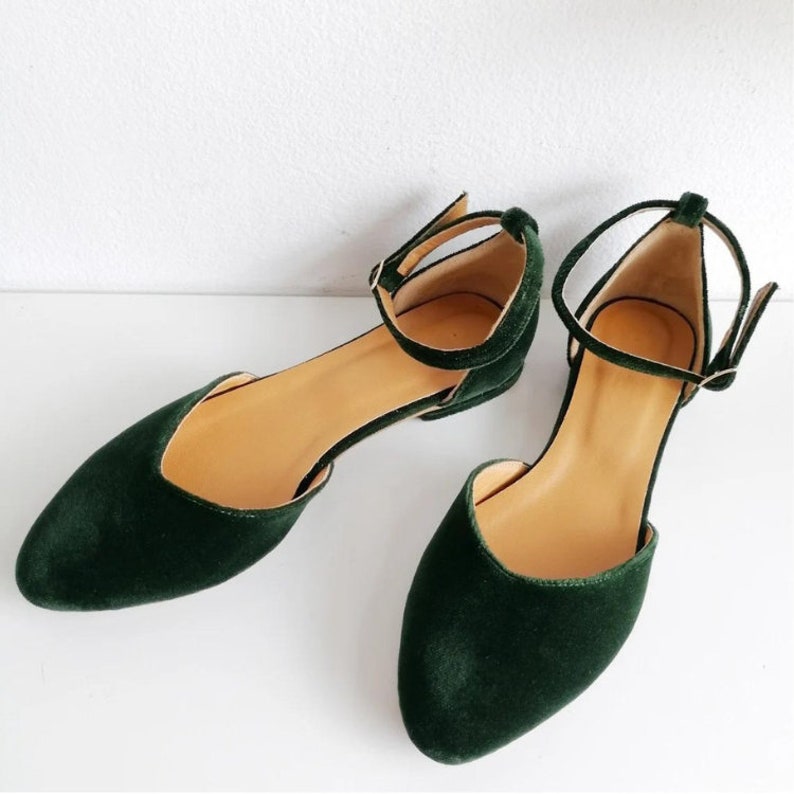 May include: A pair of dark green velvet ankle strap flats with a pointed toe.