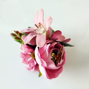 May include: A pink flower arrangement with a gold butterfly accent. The flowers are arranged in a cluster and have a delicate, feminine appearance.