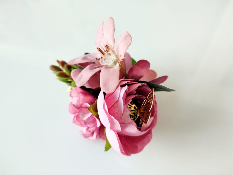 May include: A pink flower arrangement with a gold butterfly accent. The flowers are arranged in a cluster and have a delicate, feminine appearance.